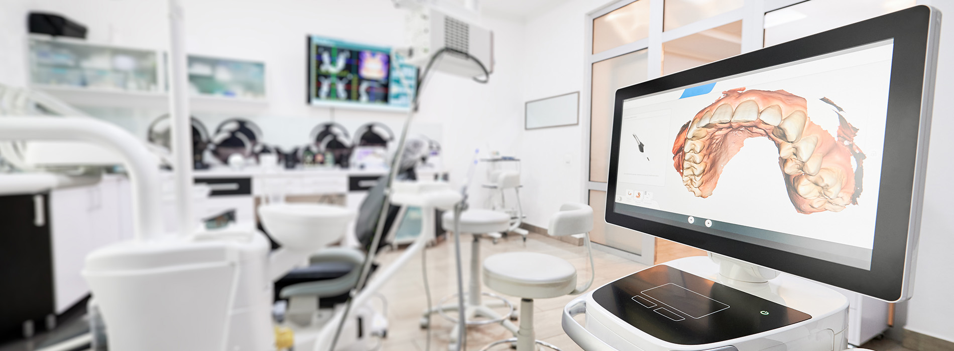 The image shows an interior view of a dental office with modern equipment, including a large screen displaying an image of a mouthpiece, multiple chairs, and various dental tools and instruments.