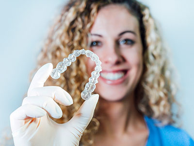 A smiling woman holding up a clear plastic dental retainer with a single tooth inside.
