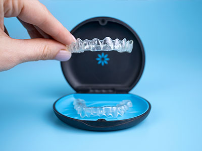 A pair of clear braces being held up by a hand, placed inside an open blue container with a white lid.