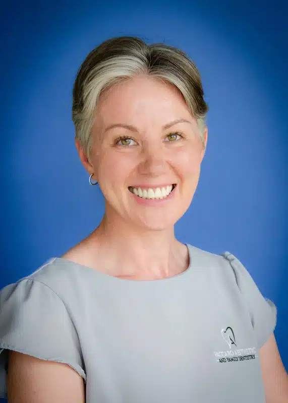 The image shows a woman posing for a portrait with a professional background, smiling at the camera.