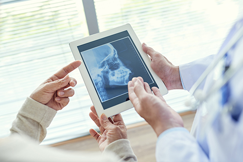 A tablet screen displaying an X-ray image being held by two people in a medical setting.