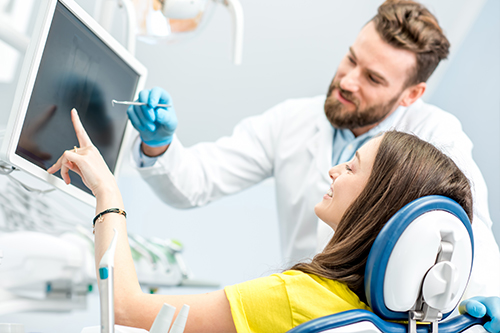 A man and woman are present in a medical setting with a large screen displaying medical imagery behind them.