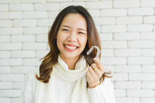 A woman holding a small object with a smile on her face, posing for a portrait against a brick wall background.