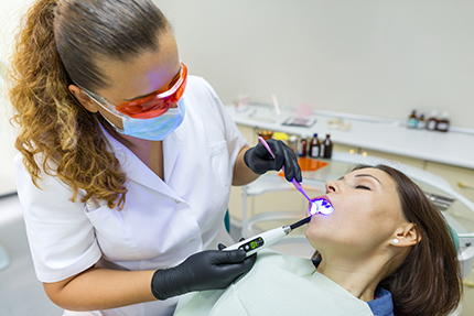 Woman dental hygienist using a dental laser on patient s teeth.