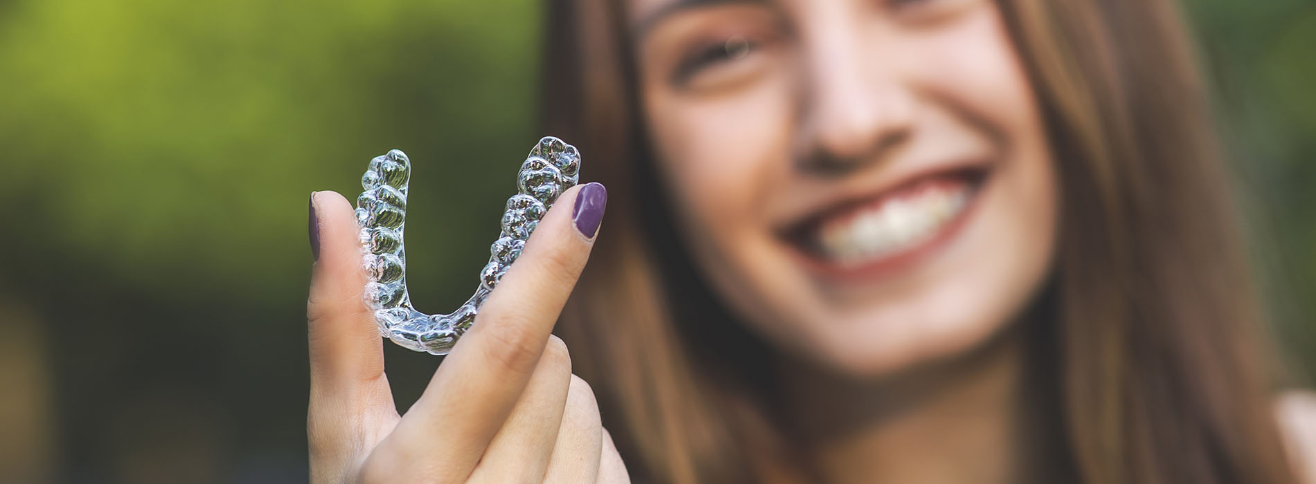 The image shows a person holding a clear plastic object with a heart shape inside, which appears to be a soap bubble, against a blurred background.